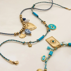 Detail of woven bracelets with turquoise beads and gold sun, heart, and evil eye charms