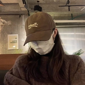 Close-up of brown baseball cap with white cursive embroidery and warm knit sweater