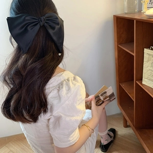 Detail of a large black satin bow hair clip with white pearls worn on long curly hair