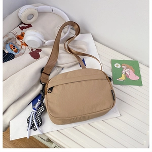 Détail du sac bandoulière en nylon kaki avec poche zippée et accessoire d'ours à damier