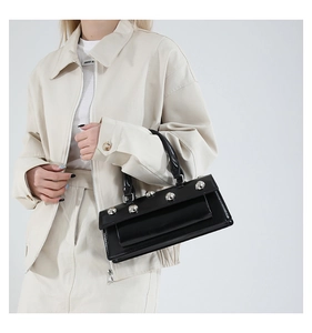 Detail of black patent leather baguette bag featuring silver studs on the flap