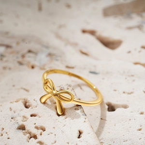 Elegant 18K gold bow knot ring displayed on a minimalist beige stone background