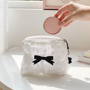 Borsa da trucco in pizzo bianco con fiocco nero e ciondolo a orso in una scena da tavolo