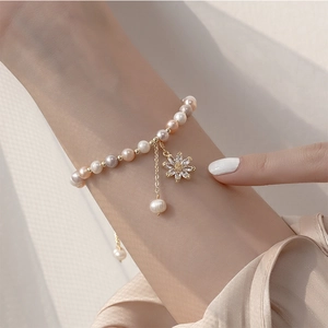 Detail of freshwater pearl bracelet with a gold sunflower charm on a model wrist