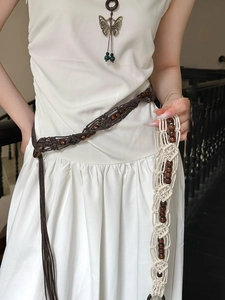 Detail of bohemian hand-woven waist belt with wooden beads and tassels on a white dress