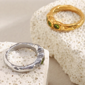 Close-up of gold and silver hammered rings with three green zircon stones on stone
