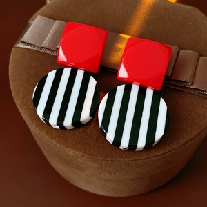 Close-up of geometric resin earrings with red square and black and white striped circle