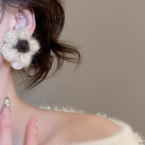 Detail view of plush flower earring in beige and brown, showing its warm knitted texture