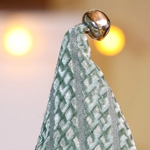 Detailaufnahme von grünem Steppstoff mit einer polierten silbernen Glocke als Deko