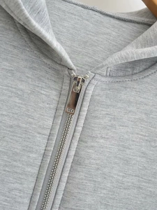 Detailed macro view of the silver metal zipper and grey knit fabric on the hoodie coat