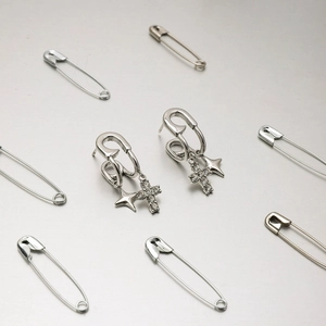 Detail of silver safety pin earrings with sparkling zircon cross and star pendants
