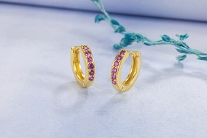 Macro detail of 14K gold plated hoop earrings with pink crystal stones on textured paper