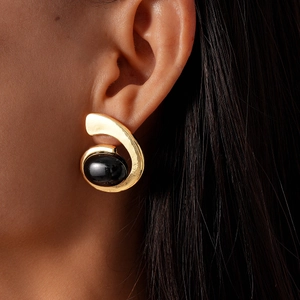 Gros plan de boucles d'oreilles dorées géométriques avec une pierre noire ovale rétro