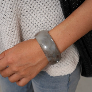 Dettaglio di un ampio bracciale in resina con venature naturali indossato da una modella