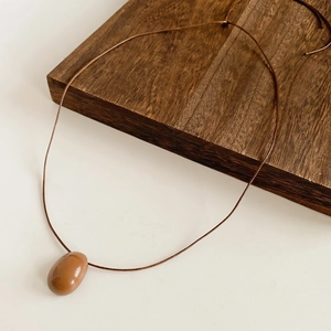 Gros plan détaillé d'un pendentif galet poli marron café sur un collier en cordon de cire