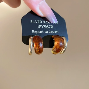 Detailed shot of C-shaped amber resin and gold metal earrings on a silver 925 card