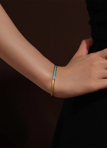 Detail of a minimalist gold bracelet with green enamel inlay worn on a model's wrist
