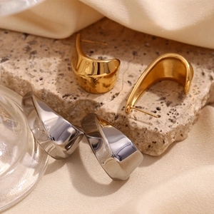 Detailed view of 18K gold and silver hollow curved earrings on a natural stone background