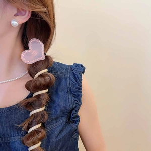 Détail d'une pince coeur rose et d'un élastique spirale beige sur une tresse élégante