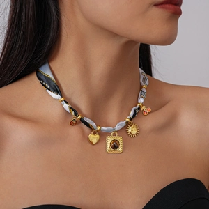 Detail of fabric scarf necklace with gold heart lock, sun face and cherry charms