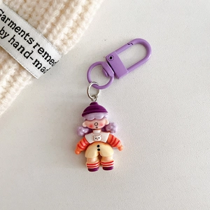 Close-up of a cartoon doll keychain with purple hat and striped top on white texture