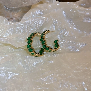 Dettaglio di orecchini a cerchio in oro a forma di C con gemme verde smeraldo su fondo bianco