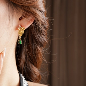 Détail des boucles d'oreilles fleur vintage dorées avec une pierre précieuse verte