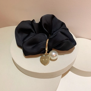 Detailed shot of black silk scrunchie with a gold heart pendant and pearl detail