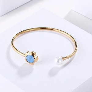 Elegant gold open bangle with light blue flower crystal and white pearl on white stand