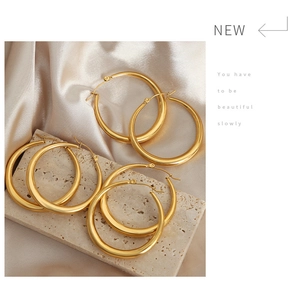 Detailed macro shot of three sizes of luxury 18K gold-plated hoop earrings on silk