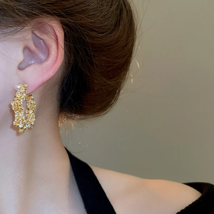 Close-up of gold irregular texture hoop earrings with sparkling crystal accents on a model