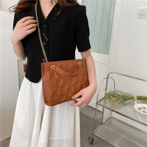 Detail of caramel brown crossbody bag with quilted rhombic texture and gold chain strap