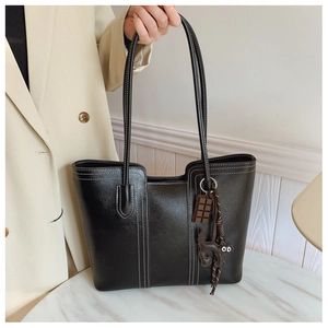 Detail of black tote bag featuring white contrast stitching and cute cat charm on marble