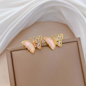 Macro shot of gold butterfly earrings with pink laser wings and crystal accents