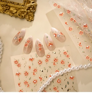 Macro view of vintage floral nail stickers with orange petals and gold leaf details