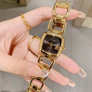 Detailed view of women's gold hollow chain watch featuring a black square dial on a wrist