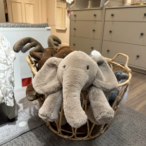 Cute gray plush elephant and brown moose toy in a woven basket for home nursery