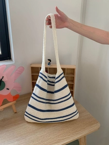 Macro detail of hand-knitted tote bag with cream and navy stripes on a wooden surface
