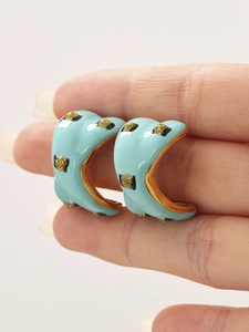 Close-up of hand holding blue enamel C-shaped earrings with gold leopard print patterns