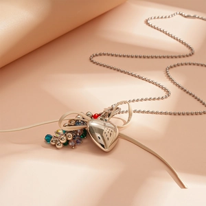 Detail of silver heart pendant with colorful beads and beige ribbon bow on bead chain