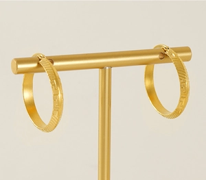 Detail of gold circular titanium steel earrings with embossed Greek key pattern