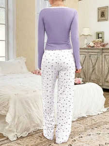 Rear view of purple women's pajamas with lace collar and crown print pants in a bedroom