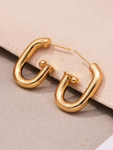 Détail macro des boucles d'oreilles en U plaquées or 18 carats sur velours beige