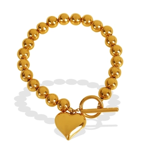 Golden beaded bracelet with heart pendant and T-bar toggle clasp on white background