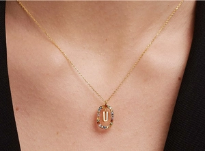 Close-up of gold chain necklace featuring oval pendant with crystal gems and letter U