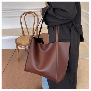 Detail of dark brown leather tote bag with long handles shown on a model's shoulder
