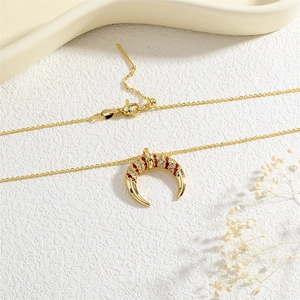 Close-up of gold crescent pendant featuring red and white zircon pavé on a white texture