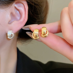 Macro detail of gold and silver brushed metal knot earrings showing textures