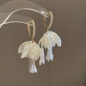 Detailed macro view of white flower earrings with pearl tassels and gold metal accents