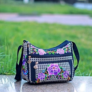 Close-up of ethnic floral embroidery on black canvas crossbody bag with silver straps